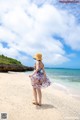 A woman in a dress and hat standing on a beach.