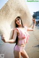 A woman in a pink bikini and a straw hat on the beach.