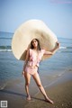 A woman in a pink bikini and a straw hat on the beach.