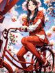 A woman sitting on a red bike in front of flowers.