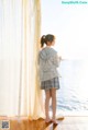 A woman standing in front of a window looking out at the ocean.