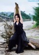 A woman in a black dress sitting on a log on the beach.