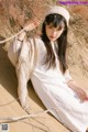 A woman in a white dress and hat sitting in the sand.