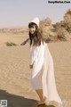 A woman in a white dress and hat standing in the sand.