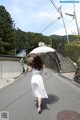 A woman in a white dress walking down a street holding an umbrella.