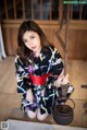 A woman in a kimono sitting on the floor holding a teapot.