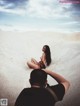 A man taking a picture of a woman sitting in the sand.