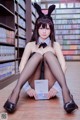 A woman sitting on the floor in front of a book shelf.