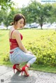 A woman in a red top and jeans crouching down on a sidewalk.