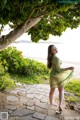 A woman in a green dress standing under a tree.