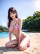 A woman in a pink bikini sitting on a beach.