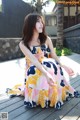 A woman sitting on a wooden deck wearing a colorful dress.