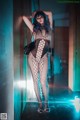 A woman in a fishnet bodysuit posing in a hallway.