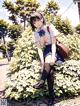 A girl in a school uniform sitting on a bush.