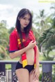 A woman in a red shirt and black shorts posing for a picture.