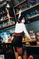 A woman standing in front of a bar holding a glass.