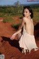 A woman in a white dress sitting on a red dirt road.