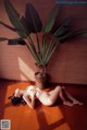 A naked woman laying on the floor next to a plant.